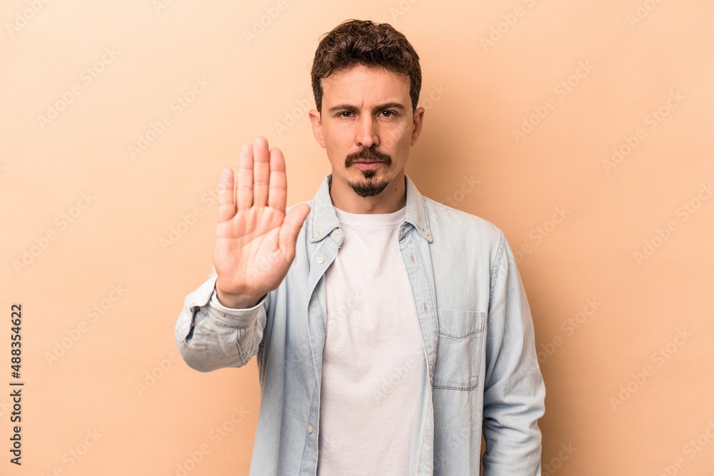 Young caucasian man isolated on beige background standing with outstretched hand showing stop sign, preventing you. Young caucasian man isolated on beige background standing with outstretched hand showing stop sign, preventing you.