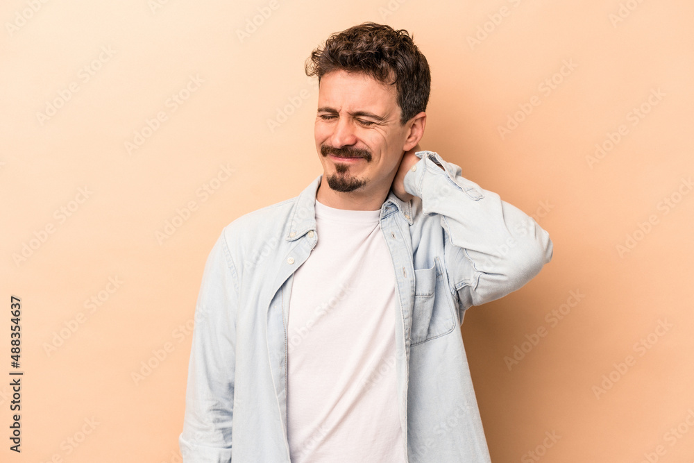 Young caucasian man isolated on beige background suffering neck pain due to sedentary lifestyle. Young caucasian man isolated on beige background suffering neck pain due to sedentary lifestyle.