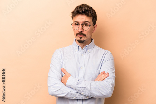 Young caucasian man isolated on beige background suspicious, uncertain, examining you.