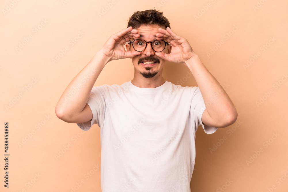 Young caucasian man isolated on beige background showing okay sign over eyes Young caucasian man isolated on beige background showing okay sign over eyes