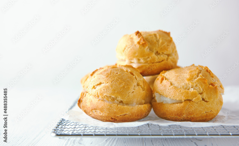 Home-made profiteroles on a metal grate on a white wooden background. Home-made profiteroles on a metal grate on a white wooden background.