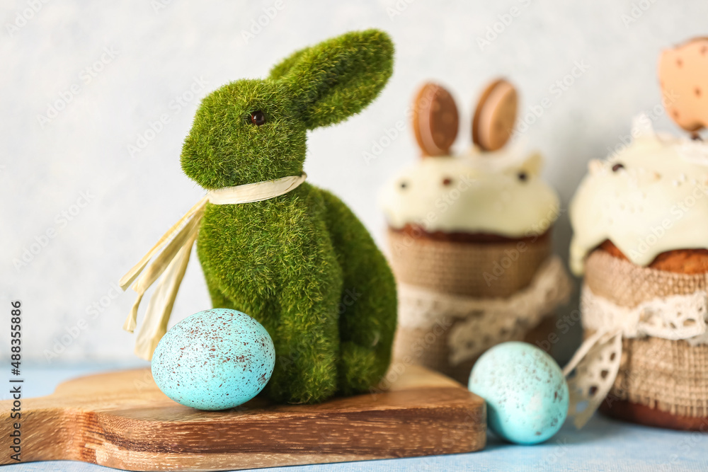 Wooden board with green Easter bunny and eggs on table