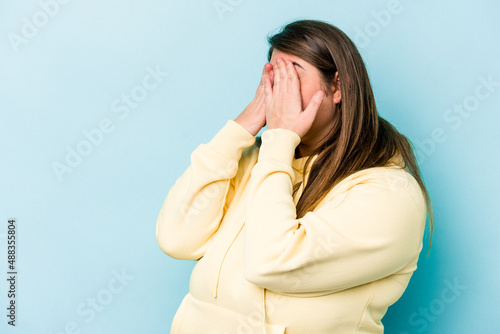 Young caucasian overweight woman isolated on blue background afraid covering eyes with hands.