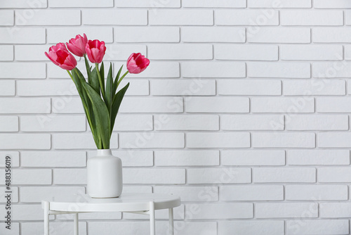 Fototapeta Naklejka Na Ścianę i Meble -  Vase with beautiful tulips on table near white brick wall
