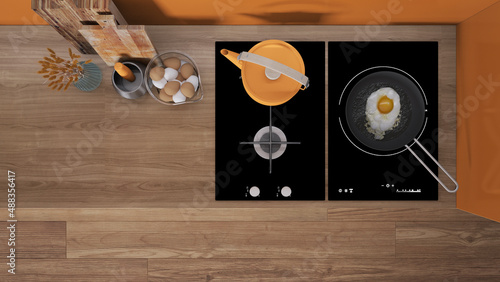 Orange and wooden kitchen close up, induction and gas hob with pot and fried egg in a pan. Vase with spikes, cutting boards. Top view, plan, above with copy space, interior design photo