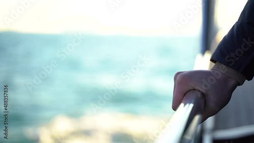 the hand of a girl in a jacket holds the railing of a boat traveling on the sea against the backdrop of the sea
