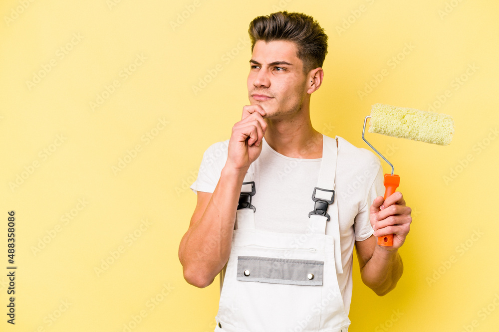Young painter man isolated on yellow background looking sideways with doubtful and skeptical expression. Young painter man isolated on yellow background looking sideways with doubtful and skeptical expression.