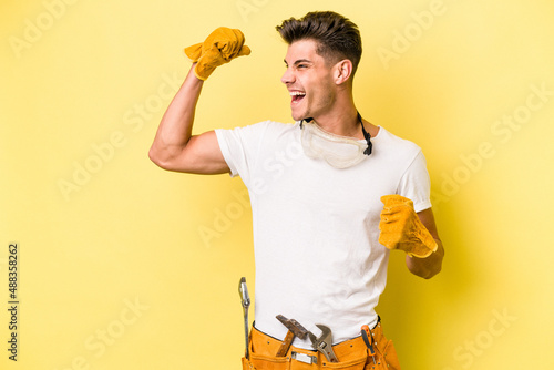 Obraz na płótnie Young electrician caucasian man isolated on yellow background raising fist after a victory, winner concept
