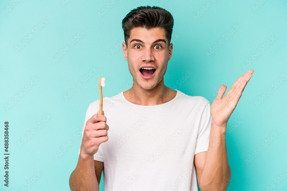 Young caucasian man brushing teeth isolated on white background surprised and shocked. Young caucasian man brushing teeth isolated on white background surprised and shocked.