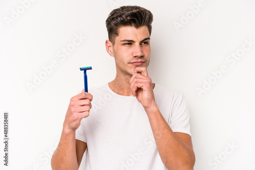 Young caucasian man shaving his beard isolated on white background looking sideways with doubtful and skeptical expression. © Asier