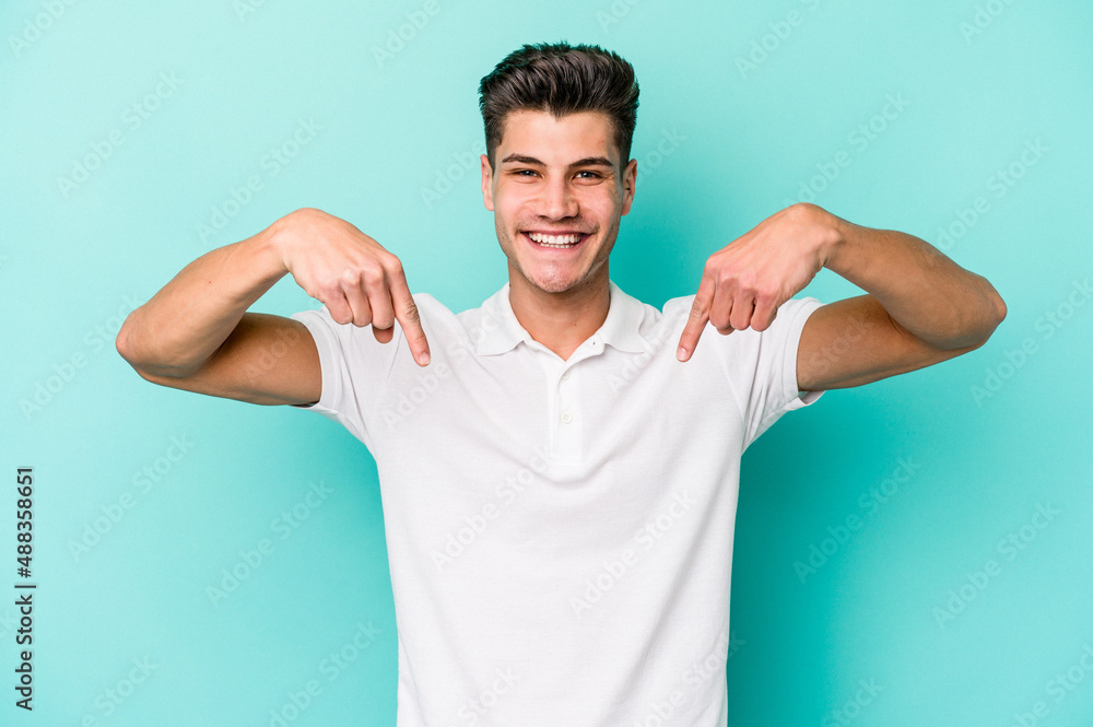 Young caucasian man isolated on blue background points down with fingers, positive feeling. Young caucasian man isolated on blue background points down with fingers, positive feeling.