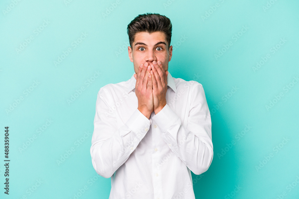 Young caucasian man isolated on blue background shocked covering mouth with hands. Young caucasian man isolated on blue background shocked covering mouth with hands.