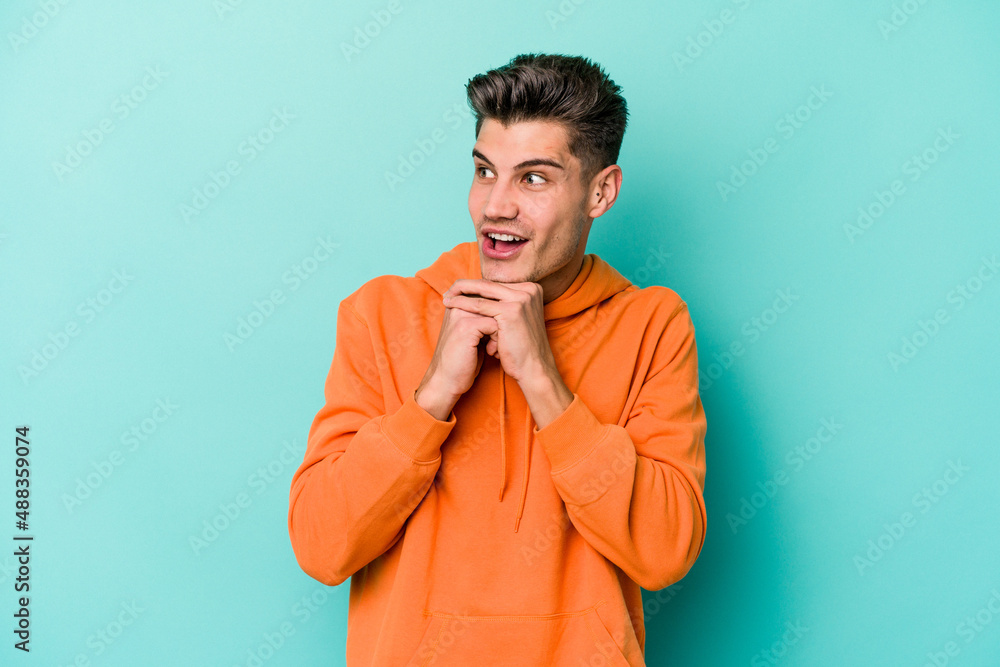 Young caucasian man isolated on blue background praying for luck, amazed and opening mouth looking to front. Young caucasian man isolated on blue background praying for luck, amazed and opening mouth looking to front.