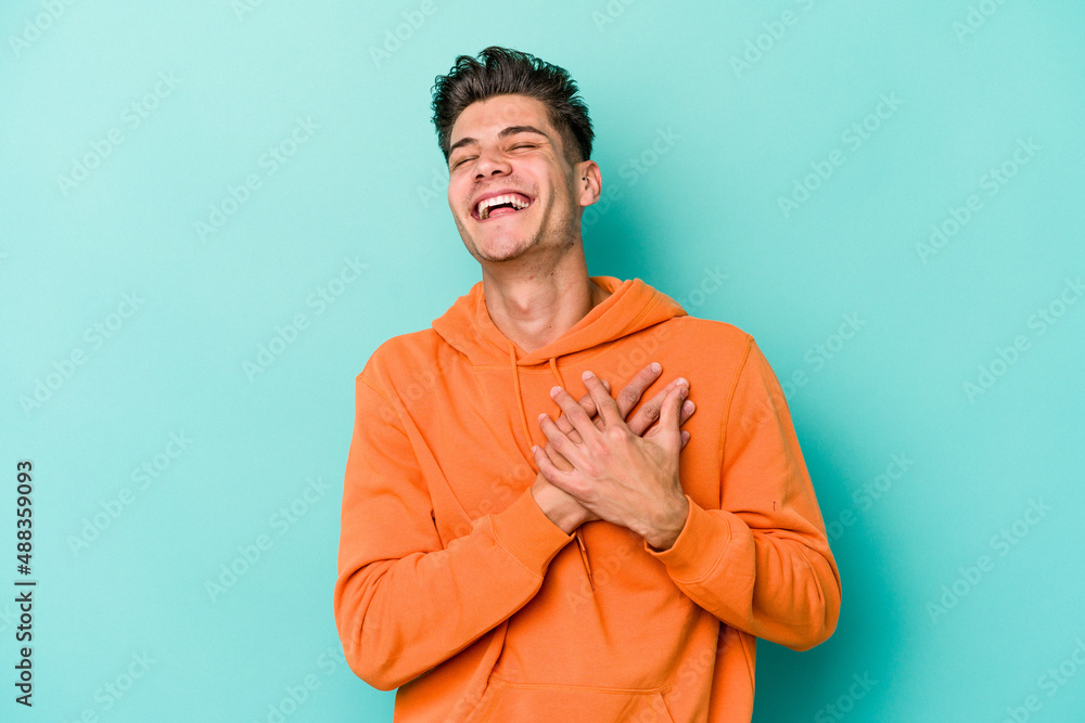 Young caucasian man isolated on blue background laughing keeping hands on heart, concept of happiness. Young caucasian man isolated on blue background laughing keeping hands on heart, concept of happiness.