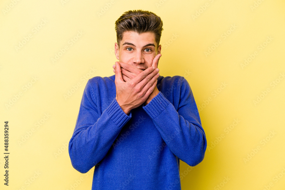 Young caucasian man isolated on yellow background shocked covering mouth with hands. Young caucasian man isolated on yellow background shocked covering mouth with hands.
