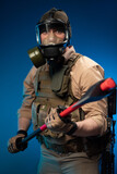 a soldier in military clothes with a bulletproof vest in a gas mask is holding a red fire axe in his hands in fright