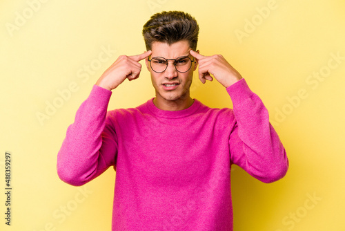 Young caucasian man isolated on yellow background focused on a task, keeping forefingers pointing head.