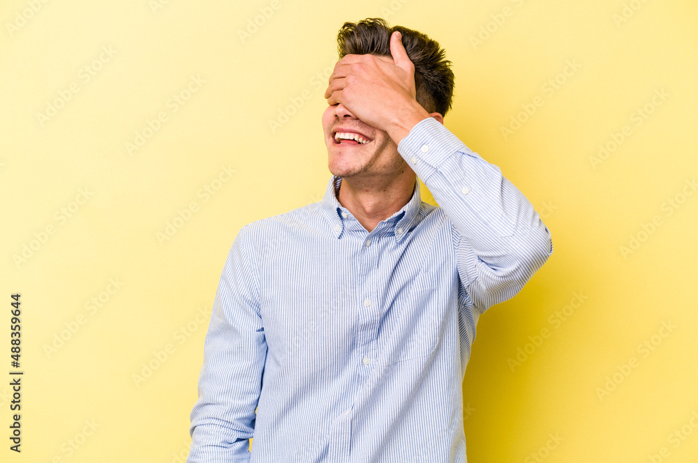 Young caucasian man isolated on yellow background covers eyes with hands, smiles broadly waiting for a surprise. Young caucasian man isolated on yellow background covers eyes with hands, smiles broadly waiting for a surprise.