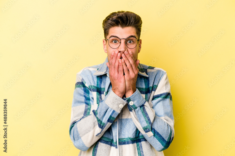 Young caucasian man isolated on yellow background shocked, covering mouth with hands, anxious to discover something new. Young caucasian man isolated on yellow background shocked, covering mouth with hands, anxious to discover something new.