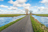 Narrow country road in a Dutch polder with ditches. The photo was taken on a sunny winter day with lots of clouds and wind in the Krimpenerwaard near the village of Ouderkerk aan den IJssel.