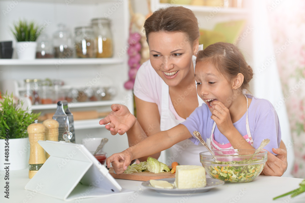 Cute little girl with her mother cooking together at kitchen table