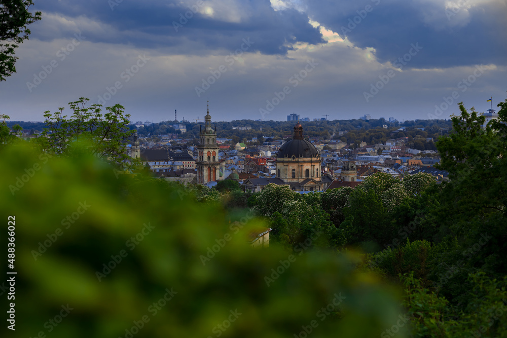 beautiful Lviv Ukrainian city panoramic view with church and town hall tower aerial photography from park land foreground unfocused foliage view, dramatic cloudy lighting