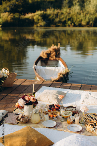 picnic on a wooden jetty near the water. a decorated picnic area awaiting guests. cheese and fruit plate on a picnic table. evening picnic party with golden sunlight.	
