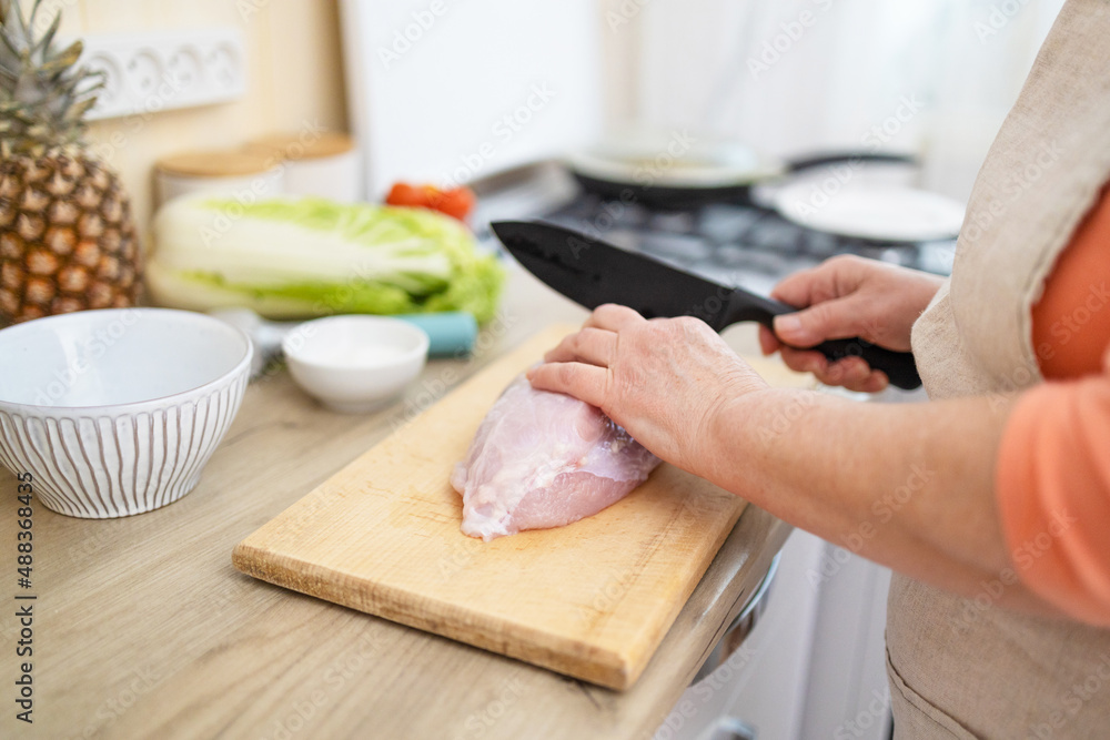 Woman is cooking in home kitchen. Female hands cut fresh Turkey meat on table on wooden boards. Ingredients for preparing food.