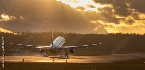 Aircraft landing at Stuttgart Airport, landing gear down, against golden sunset sky with some clouds, partly blurred by heat of jet engines