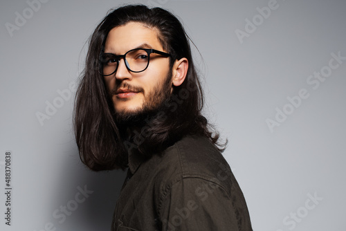 Portrait of young confident handsome man with long hair, wearing glasses.