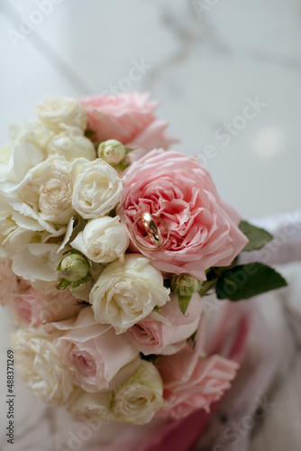 Delicate wedding bouquet of pink and white roses and wedding rings on it 