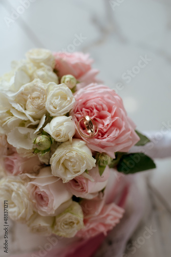 Delicate wedding bouquet of pink and white roses and wedding rings on it 