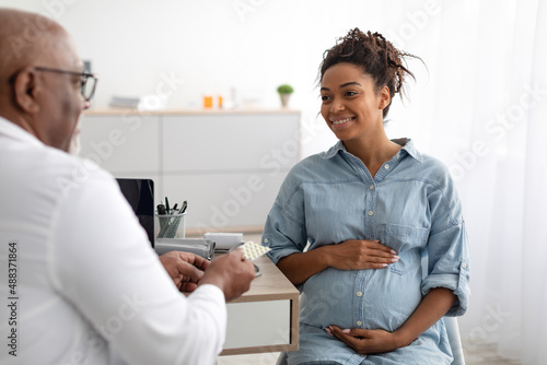 Mature experienced black doctor showing pills to pregnant lady