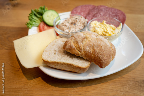 German breakfast plate with crispy bread roll, cheese, sausage and creamy spreads on a wooden table, selected focus