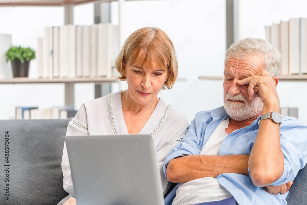 Portrait of Worried senior couple checking their bills and work on netbook read document information at home, Serious retired elderly old family reading documents with laptop