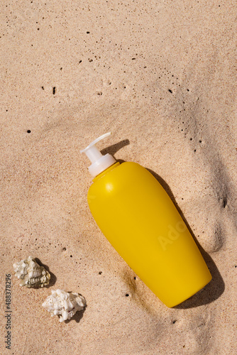 Yellow tube of suncream and seashells on the sand. UV and sunburn protection concept.