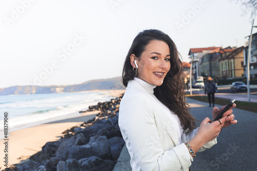 Young caucasian woman using a smartphone at the sea promenade of Hendaia, Basque Country.