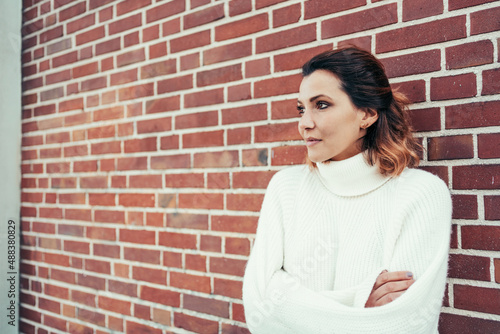 Romantic woman looking away with nostalgia against a brick wall