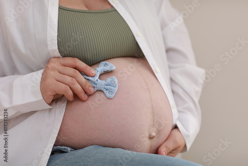 close up hands on pregnant mother holding baby clothes, two blue bows. Lover woman waiting child. Preparation for childbirth, Girl big belly advanced pregnancy photo