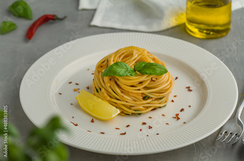 Spaghetti aglio e olio spaghetti aglio olio e peperoncino white plate lemon basil chili flakes parsley grey background photo