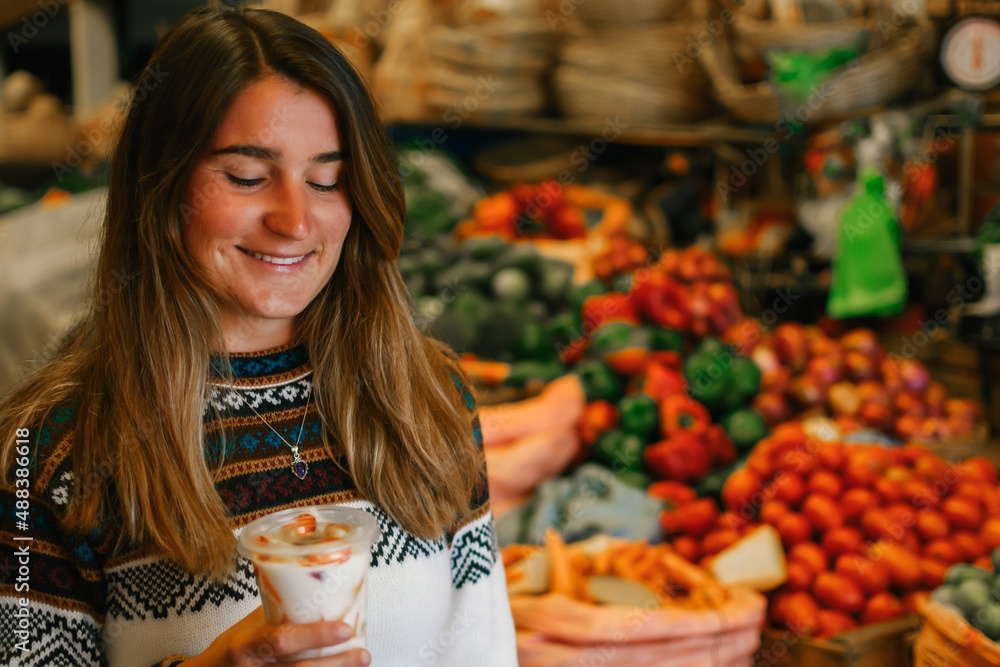 Portrait of a caucasian woman with jumper and smiling while holding a fruit salad and standing in the market Portrait of a caucasian woman with jumper and smiling while holding a fruit salad and standing in the market