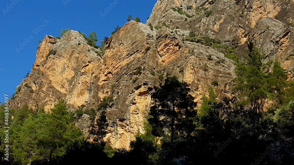 late afternoon warm sunlight on the steep mountain cliffs with a bright blue cloudless sky