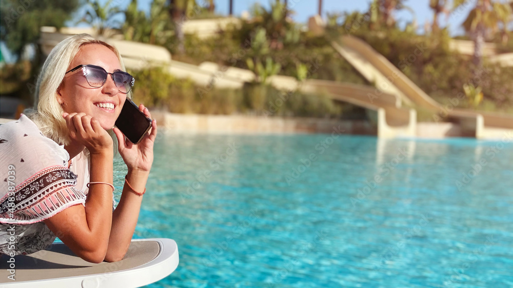 Smiling woman talking to phone on a sunbed near the pool. Copy space Smiling woman talking to phone on a sunbed near the pool. Copy space