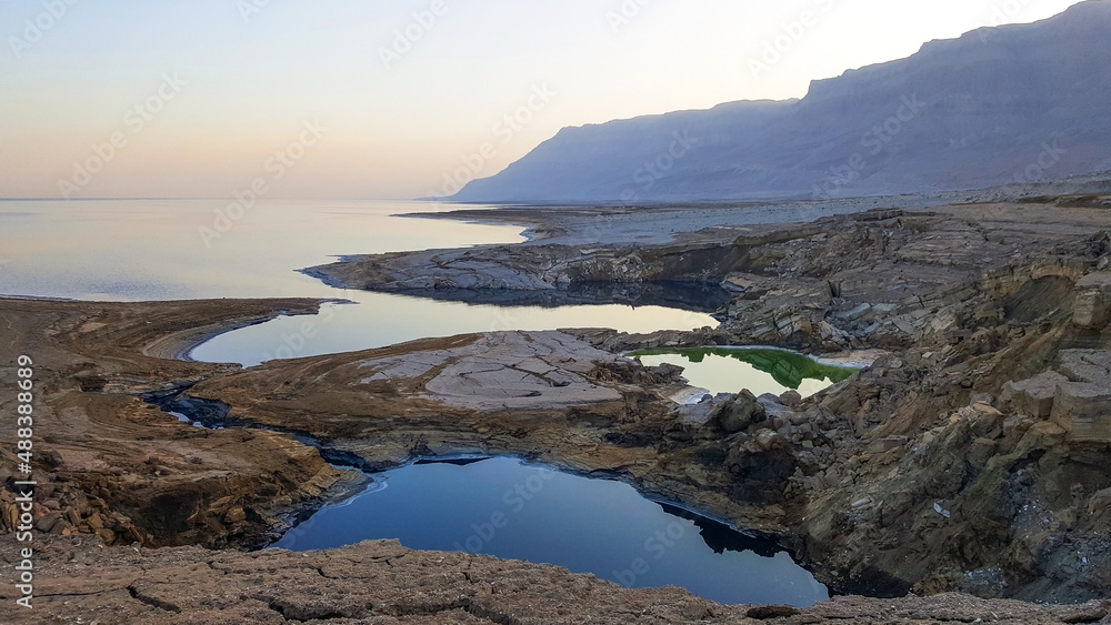 View of Dead Sea coastline. Salt crystals at sunset. Texture of Dead sea. Salty sea shore. Landscape Dead Sea coastline with natural relief channels in summer day,  failures of the soil
