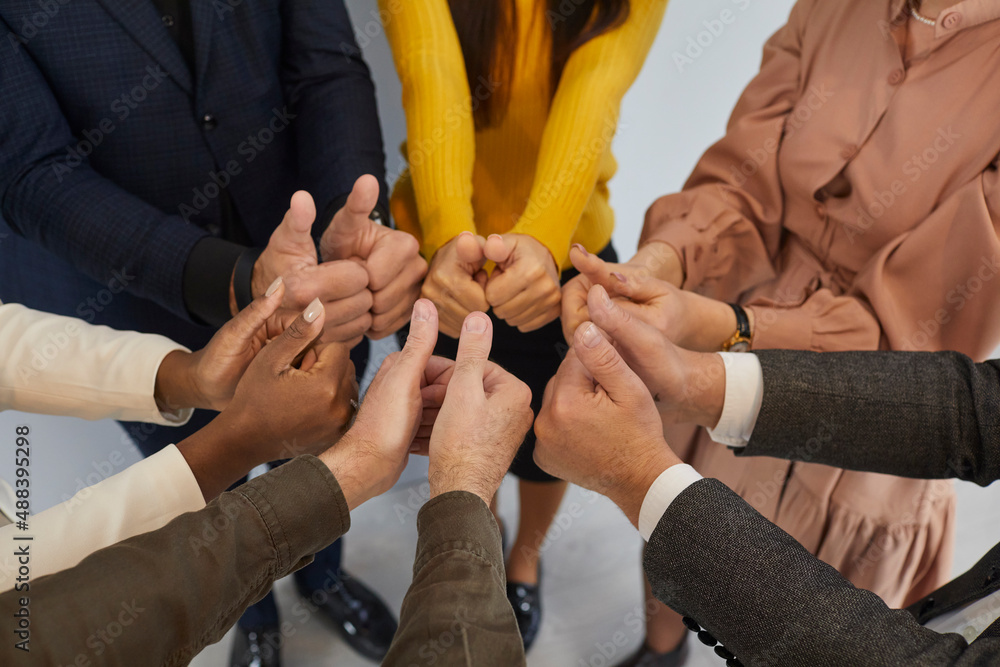 Teamwork, team, cooperation and success. Hands of successful multiracial business team standing in circle and showing thumbs up. Close up of hands of colleagues demonstrating unity and support.