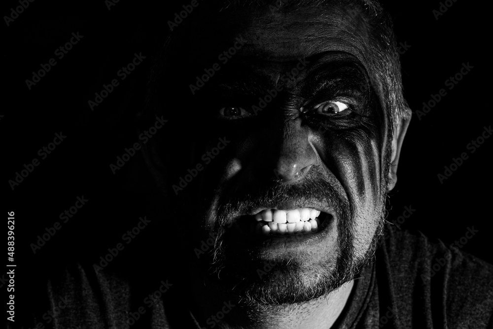 Fototapeta premium Viking man with a furious gaze and a painted face looks into the darkness with bright eyes