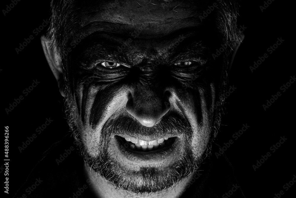 Viking man with a furious gaze and a painted face looks into the darkness with bright eyes Viking man with a furious gaze and a painted face looks into the darkness with bright eyes