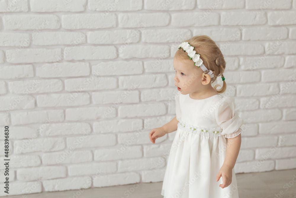 Baby child with hearing aids and cochlear implants on white brick wall with copy space and place for advertising . Deaf and health concept Baby child with hearing aids and cochlear implants on white brick wall with copy space and place for advertising . Deaf and health concept