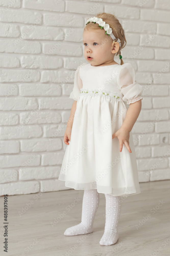 Baby child with hearing aids and cochlear implants on white brick wall. Deaf and health concept Baby child with hearing aids and cochlear implants on white brick wall. Deaf and health concept