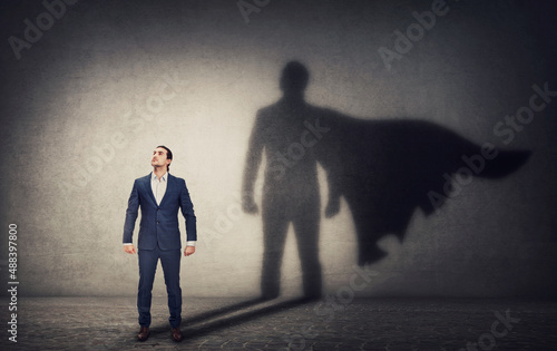 Determined businessman stands confident in a hero stance and casting a brave superhero shadow on the wall behind. Business leadership and motivation concept. Ambition and strength symbols photo